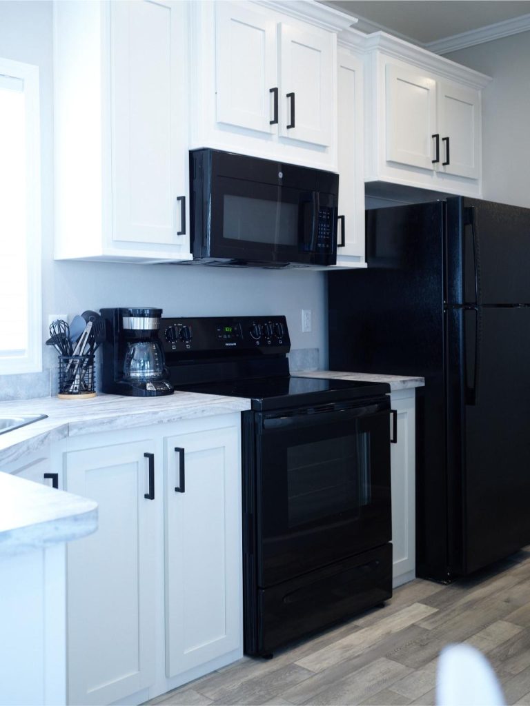 Modern kitchen with white cabinets, black appliances including a stove, microwave, refrigerator, and coffee maker, and gray countertops.